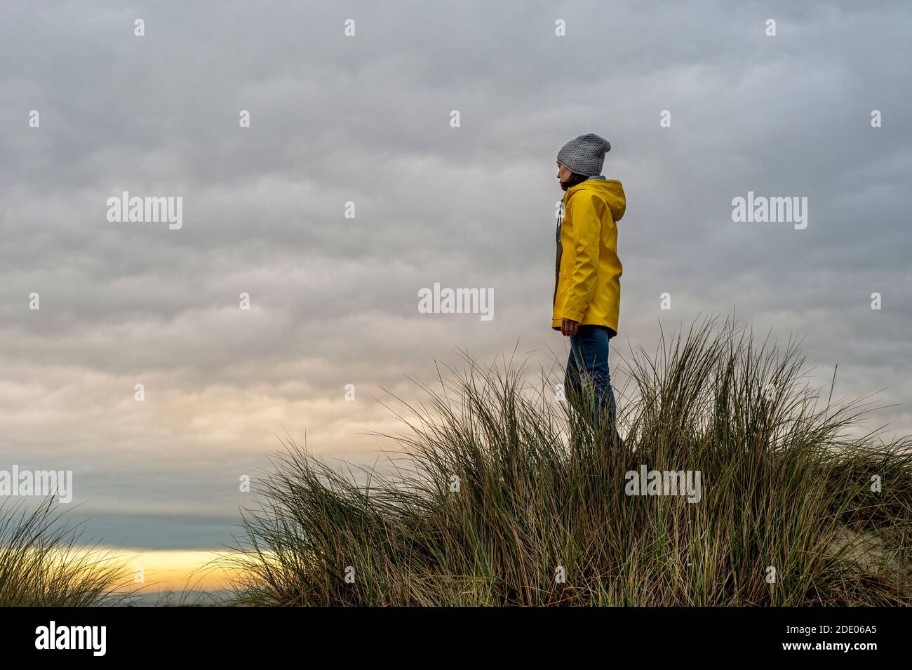 donna che indossa un cappotto giallo in piedi sulla cima di una duna, concetto di copertina del libro. Foto Stock