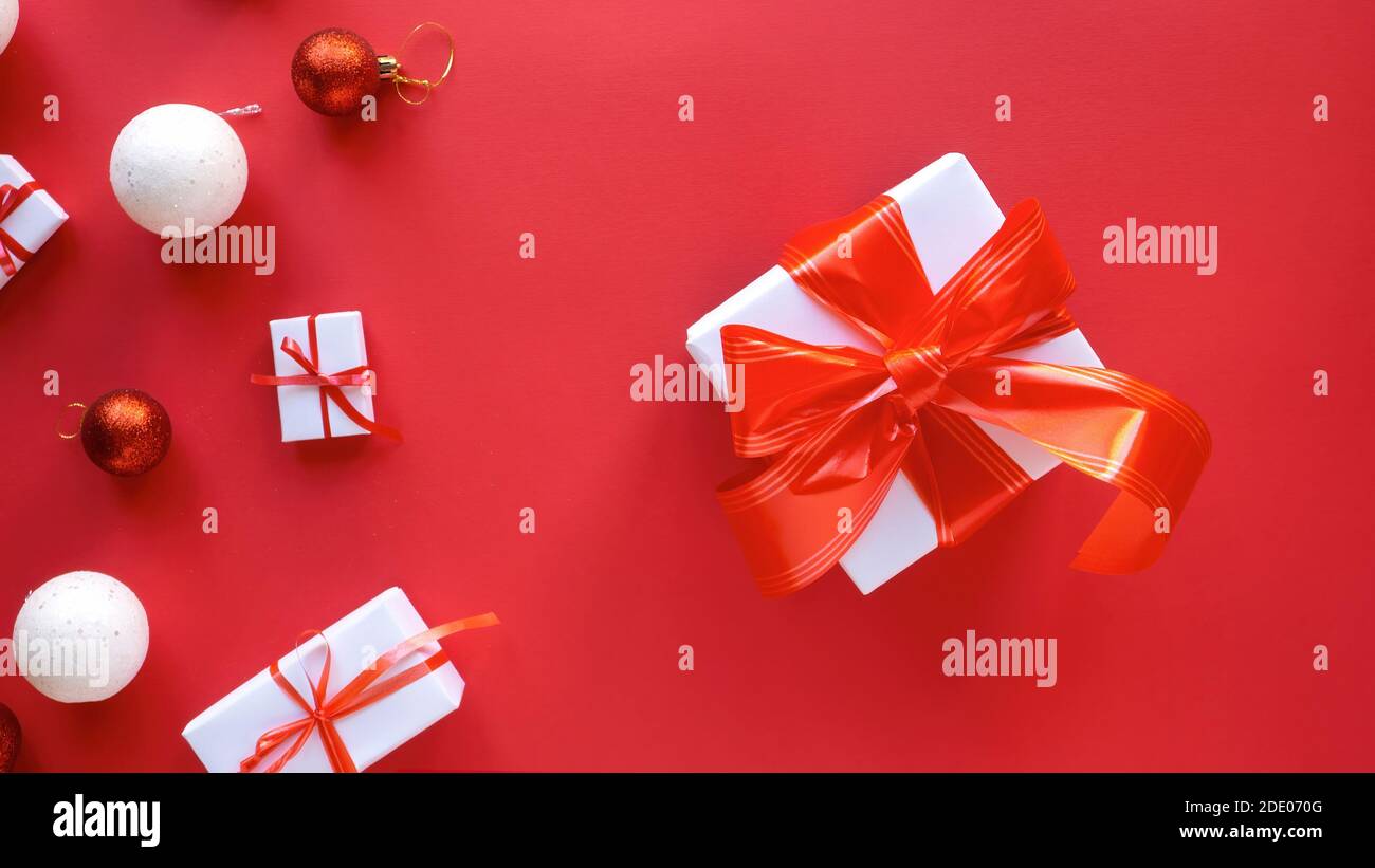 Confezioni regalo bianche multiple con nastri rossi e decorazioni natalizie su sfondo rosso. Vista dall'alto Foto Stock