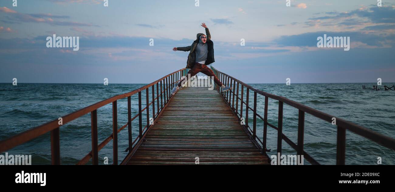 Salto pazzo di giovane uomo al molo in mare Foto Stock