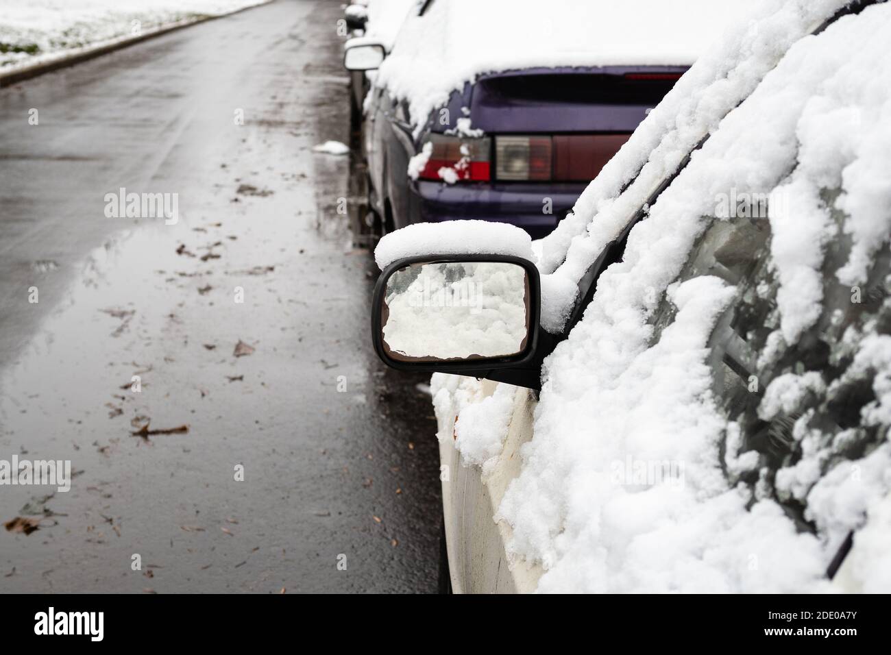 la prima neve copre le auto parcheggiate lungo la strada della città freddo giorno d'autunno (focalizzato sullo specchietto retrovisore esterno) Foto Stock