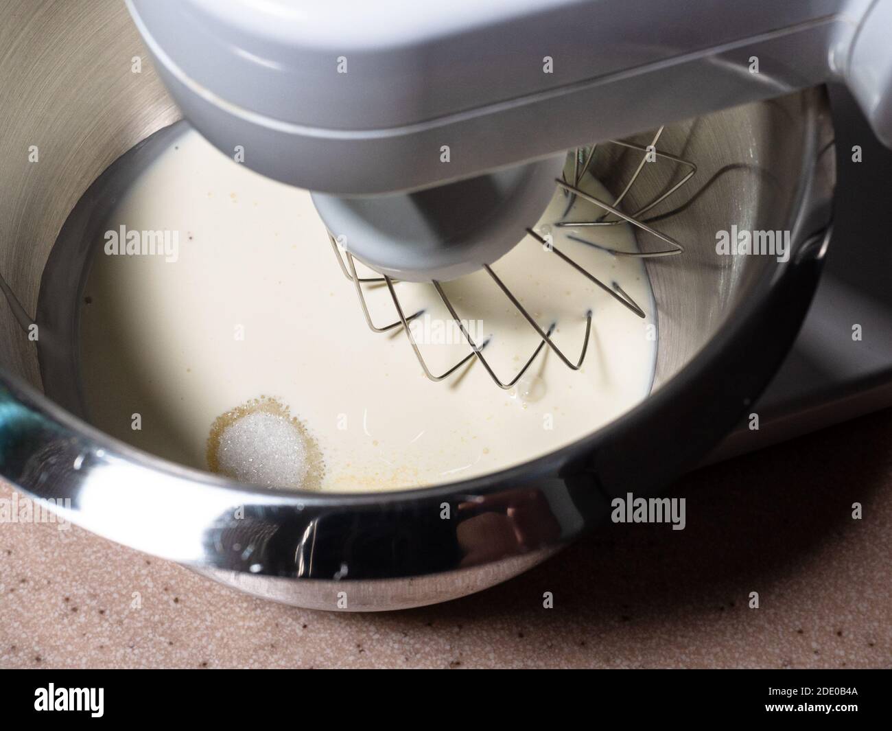 cottura dolce pan di spagna a casa - sopra la vista di crema liquida con una manciata di zucchero in una ciotola di acciaio di robot da cucina a casa Foto Stock