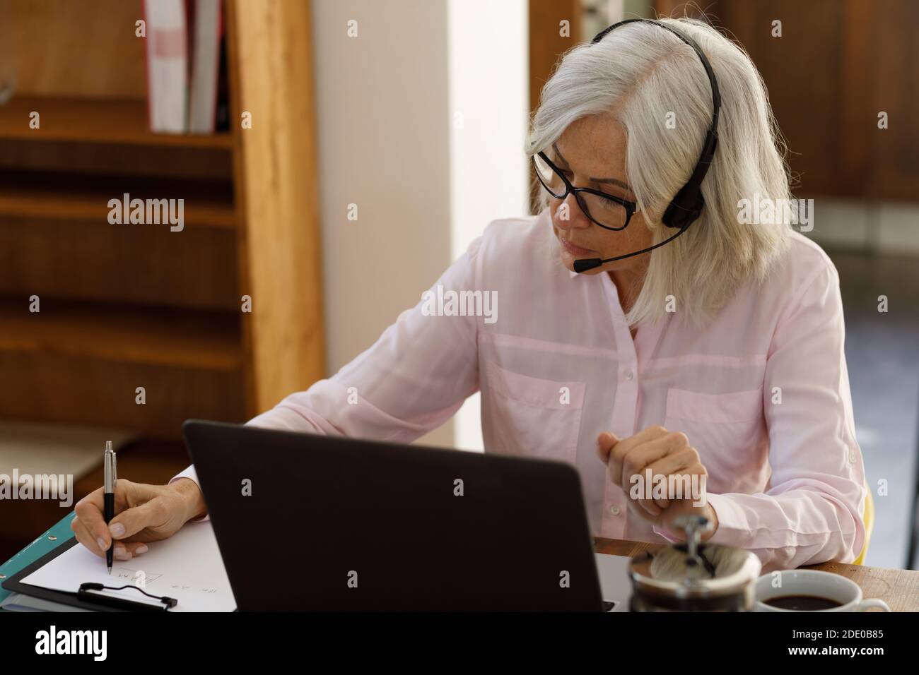 Donna caucasica anziana che usa un computer portatile e indossa le cuffie Foto Stock