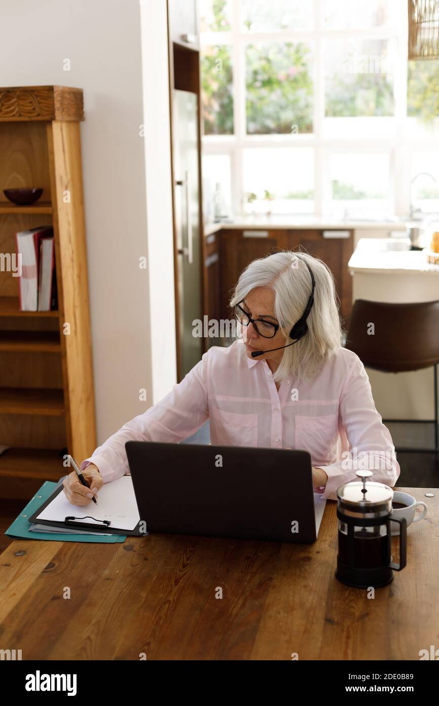Donna caucasica anziana che usa un computer portatile e indossa le cuffie Foto Stock