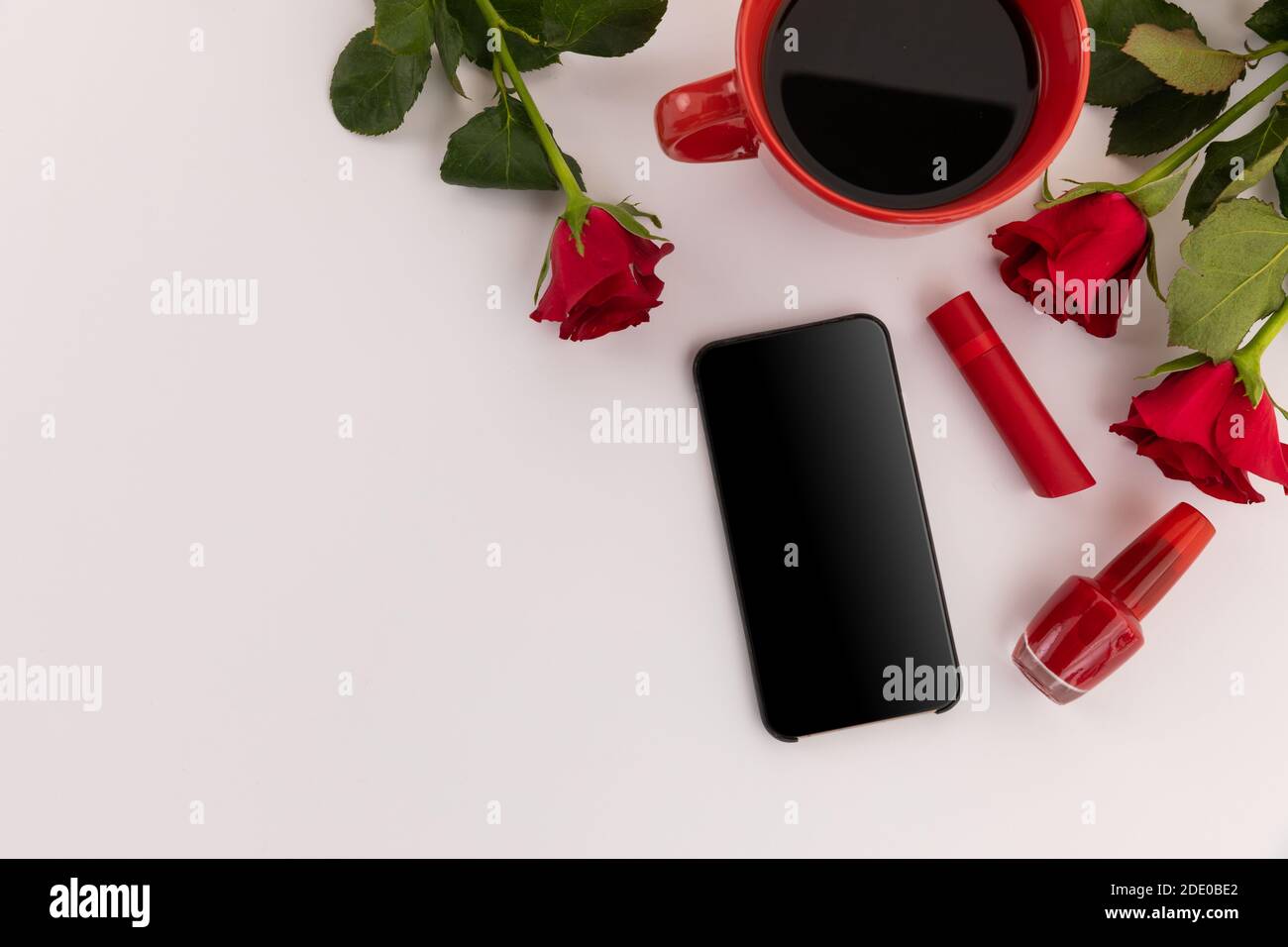 Smartphone, rossetto rosso, vernice per unghie, caffè e rose su sfondo bianco Foto Stock