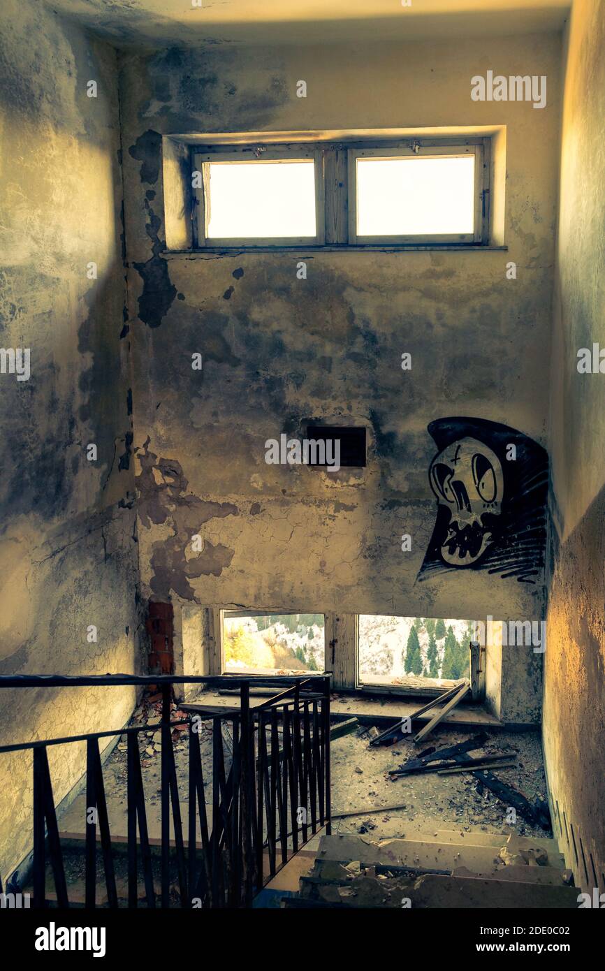 Scalinata distrutta, pareti graffite ammuffite, finestre apribili. Interno di un edificio abbandonato in rovina. Monte Grappa, Vicenza, Italia Foto Stock