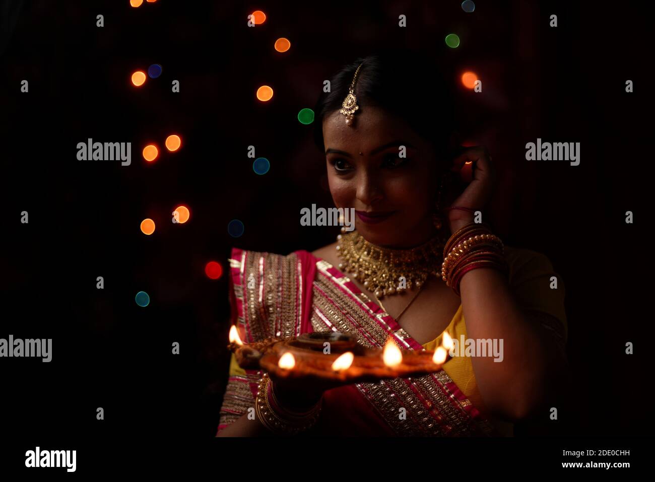 Una giovane e bella donna indiana bengalese in abito tradizionale indiano sta tenendo una Diwali diya / lampada in mano davanti a colorate luci bokeh. Foto Stock