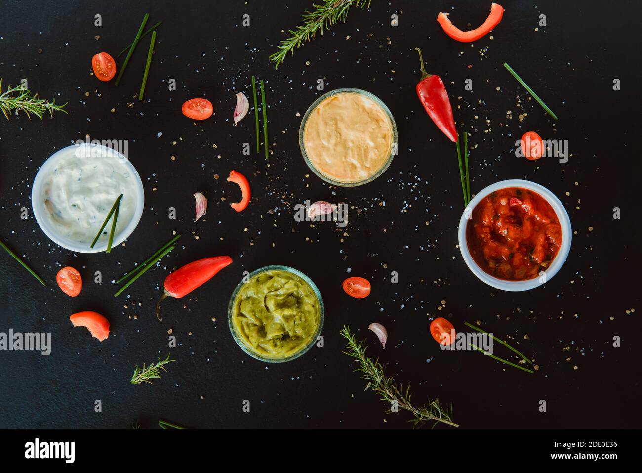 Ciotole con vista dall'alto con crema acida mayo, salsa, guacamole, salse da immersione con ingredienti e spezie su fondo nero. Salti per medicazione Foto Stock