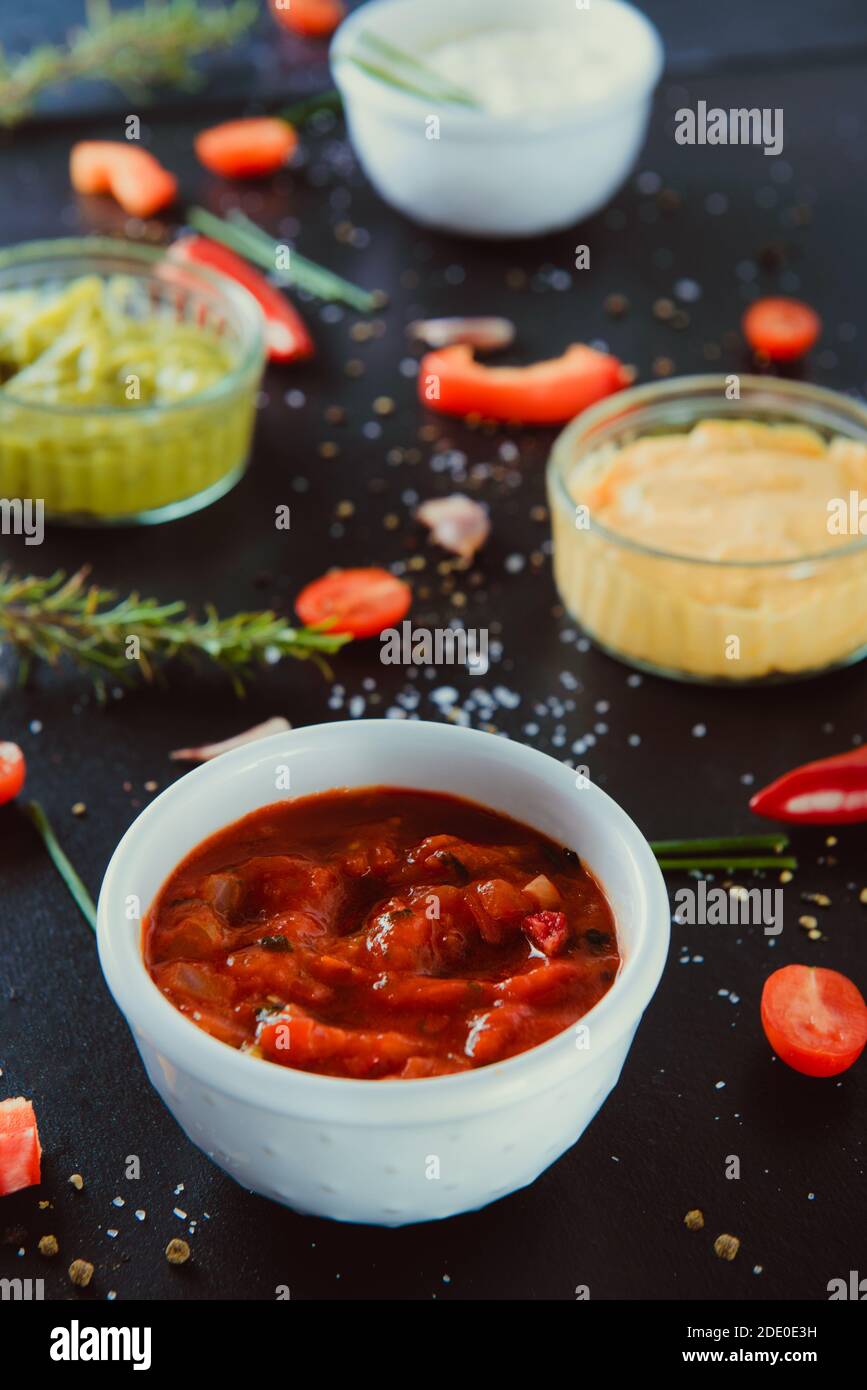 Primo piano ciotola con salsa sause con mayo panna acida, guacamole, salse da immersione al formaggio con ingredienti e spezie su fondo nero. Medicazione Foto Stock