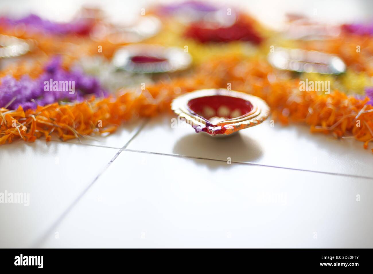 Bellissimi rangoli sacri preparati da vivaci fiori colorati e lampade decorative colorate a pavimento bianco. Stile di vita indiano e celebrazione di Diwali Foto Stock