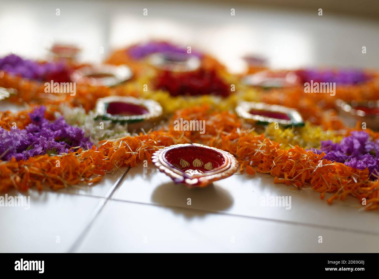 Bellissimi rangoli sacri preparati da vivaci fiori colorati e lampade decorative colorate a pavimento bianco. Stile di vita indiano e celebrazione di Diwali Foto Stock