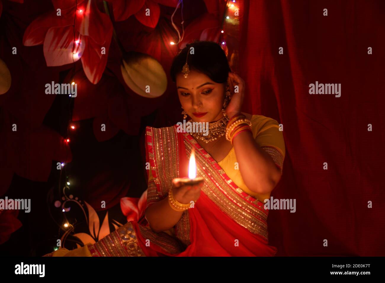 Una giovane e bella donna indiana bengalese in abito tradizionale indiano sta tenendo una Diwali diya / lampada in mano davanti a colorate luci bokeh. Foto Stock