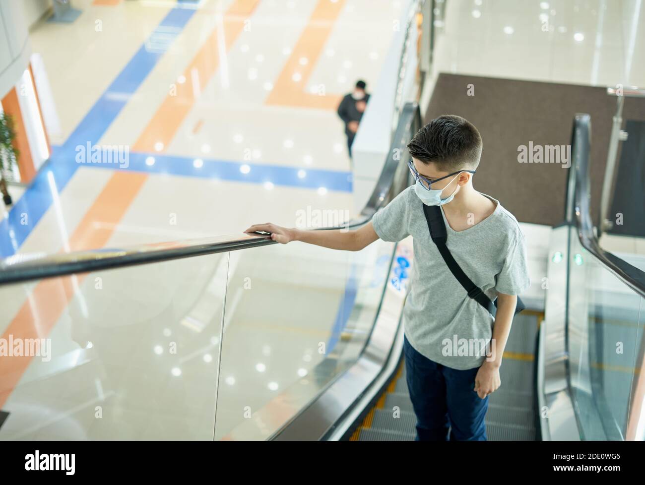 Ragazzo adolescente che indossa la maschera sulla scala mobile nel centro commerciale Foto Stock