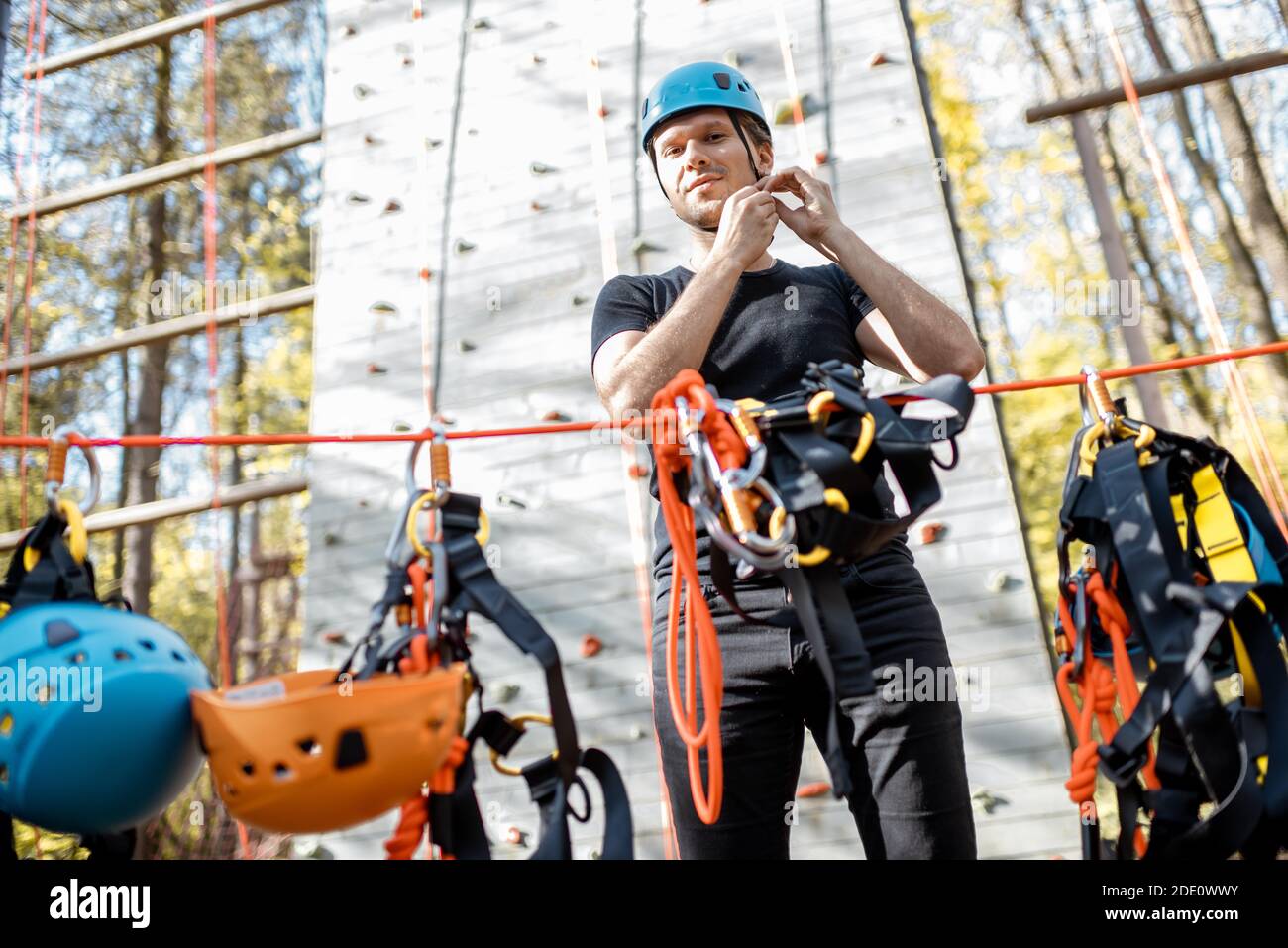 Bell'uomo che indossa attrezzature di sicurezza per l'arrampicata al parco divertimenti, preparandosi per l'arrampicata sulla parete Foto Stock