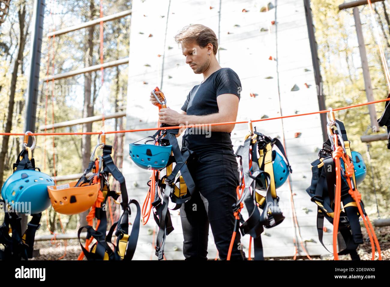 Bell'uomo che indossa attrezzature di sicurezza per l'arrampicata al parco divertimenti, preparandosi per l'arrampicata sulla parete Foto Stock