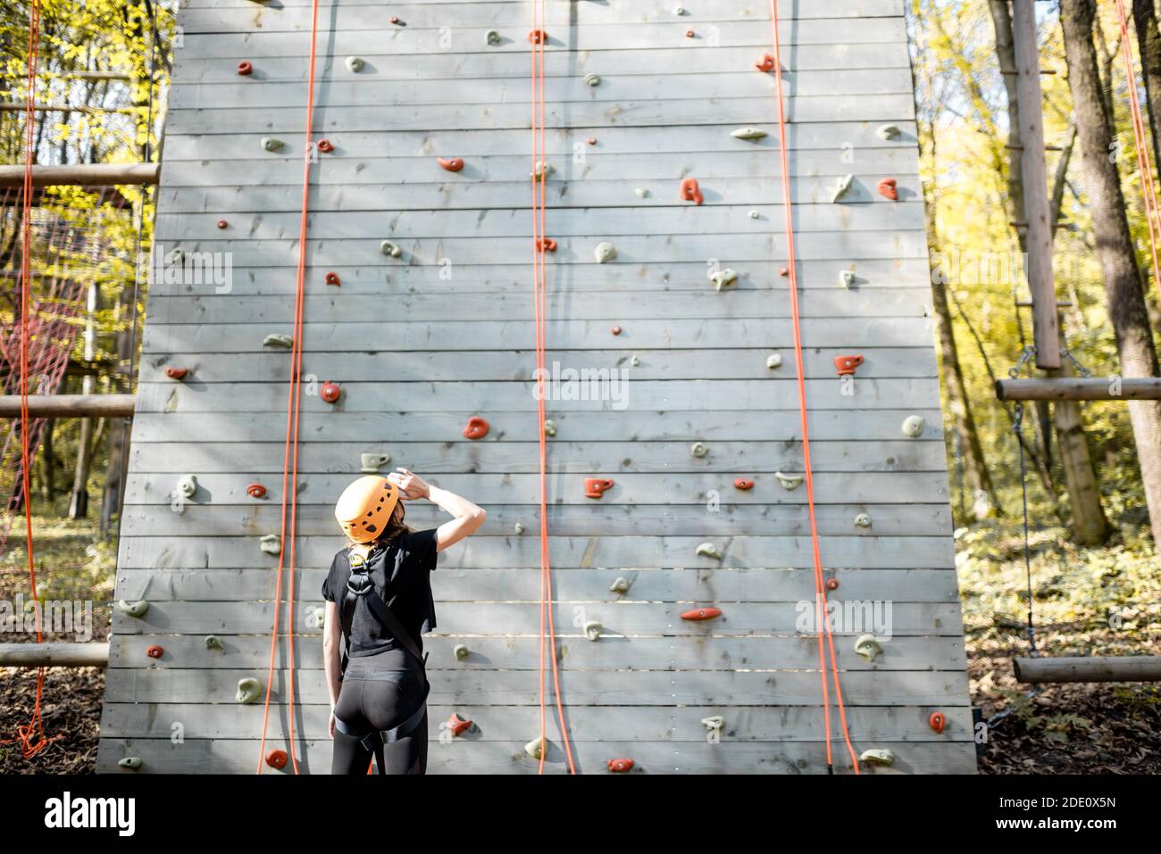 Giovane donna in abbigliamento sportivo e di sicurezza che guarda sulla parete di arrampicata prima di salire. Ampia vista dal retro Foto Stock