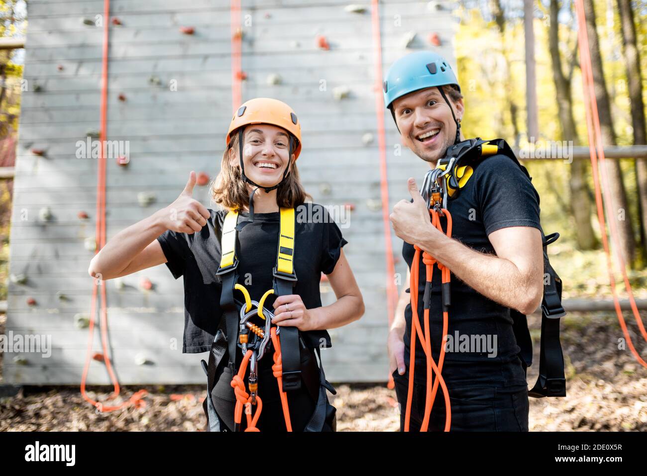 Ritratto di una giovane coppia ben attrezzata con equipaggiamento di sicurezza stare insieme di fronte alla parete di arrampicata al divertimento parcheggio Foto Stock