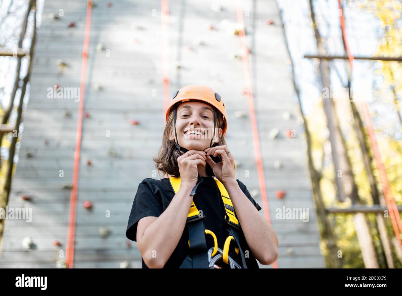 Ritratto di una giovane donna ben attrezzata in piedi davanti della parete di arrampicata al parco divertimenti Foto Stock