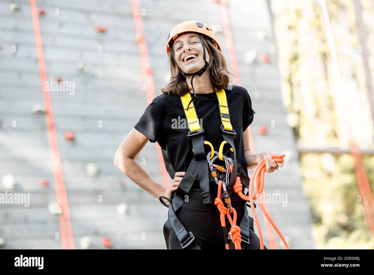 Ritratto di una giovane donna ben attrezzata in piedi davanti della parete di arrampicata al parco divertimenti Foto Stock