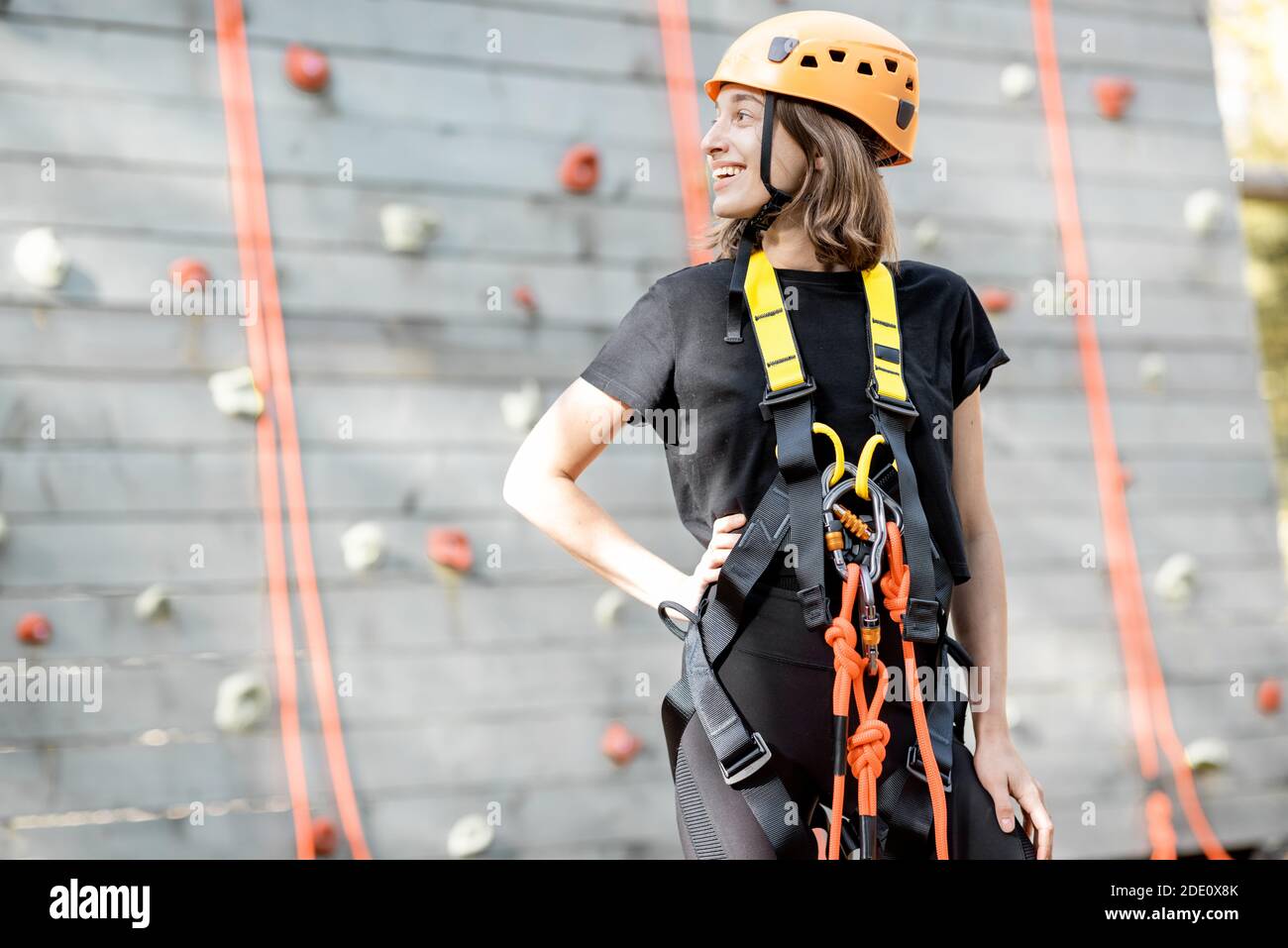 Ritratto di una giovane donna ben attrezzata in piedi davanti della parete di arrampicata al parco divertimenti Foto Stock
