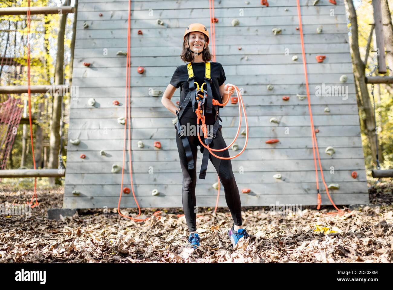 Ritratto a lunghezza intera di una giovane donna ben attrezzata in piedi di fronte alla parete di arrampicata del parco divertimenti Foto Stock