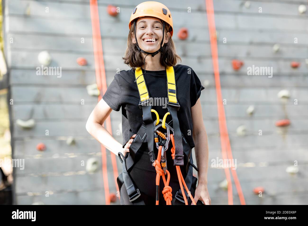 Ritratto di una giovane donna ben attrezzata in piedi davanti della parete di arrampicata al parco divertimenti Foto Stock