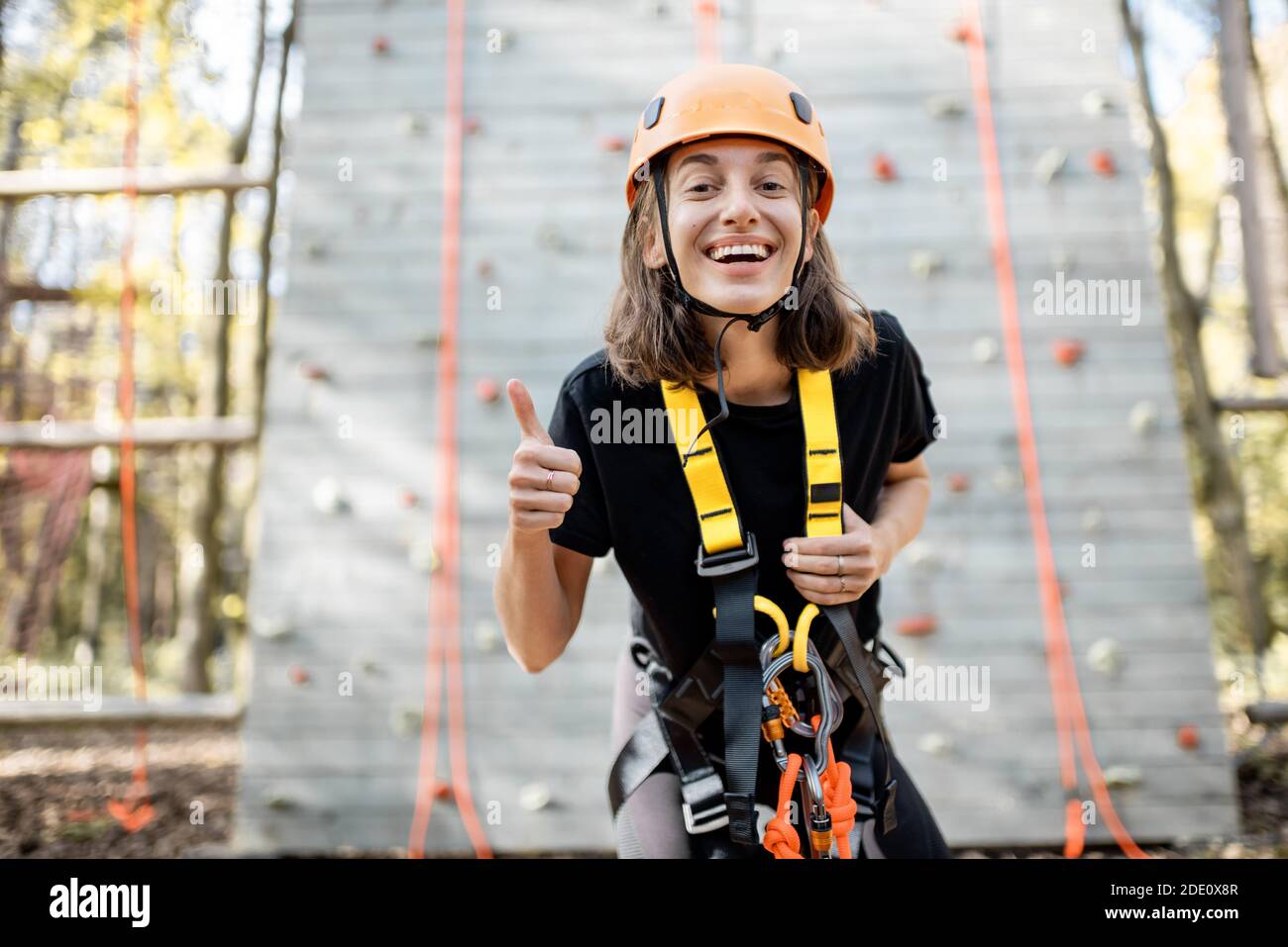 Ritratto di una giovane donna ben attrezzata in piedi davanti della parete di arrampicata al parco divertimenti Foto Stock