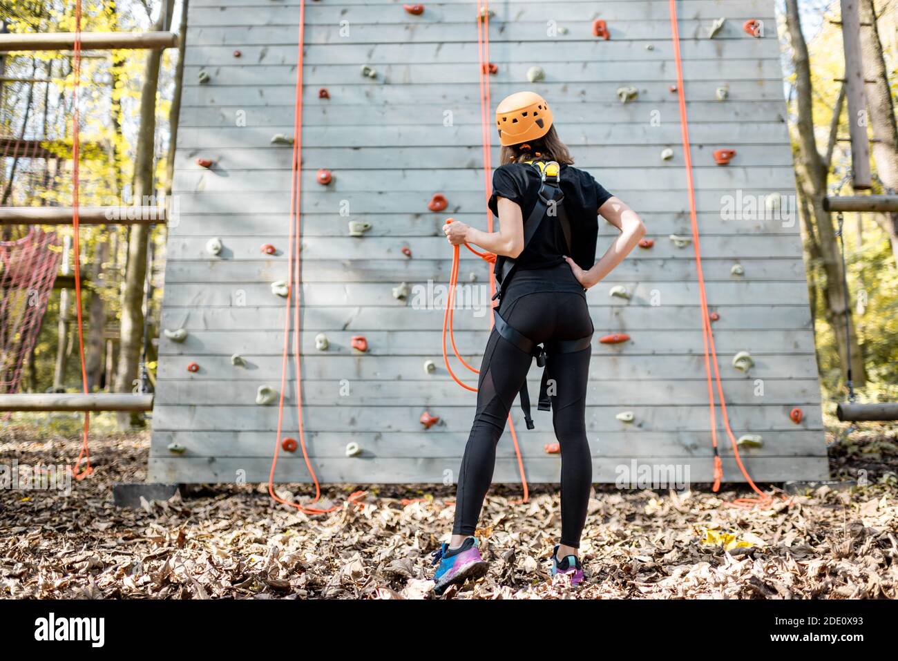 Giovane donna in abbigliamento sportivo e di sicurezza che guarda sulla parete di arrampicata prima di salire. Vista dal retro Foto Stock