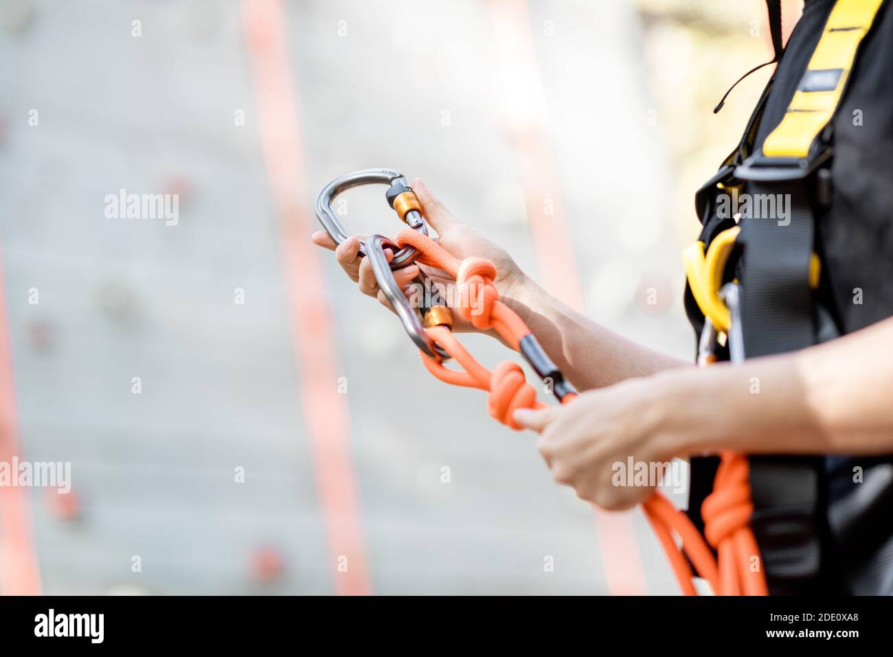 Primo piano delle attrezzature di sicurezza per gli scalatori indossati sulla donna con parete di arrampicata sullo sfondo Foto Stock