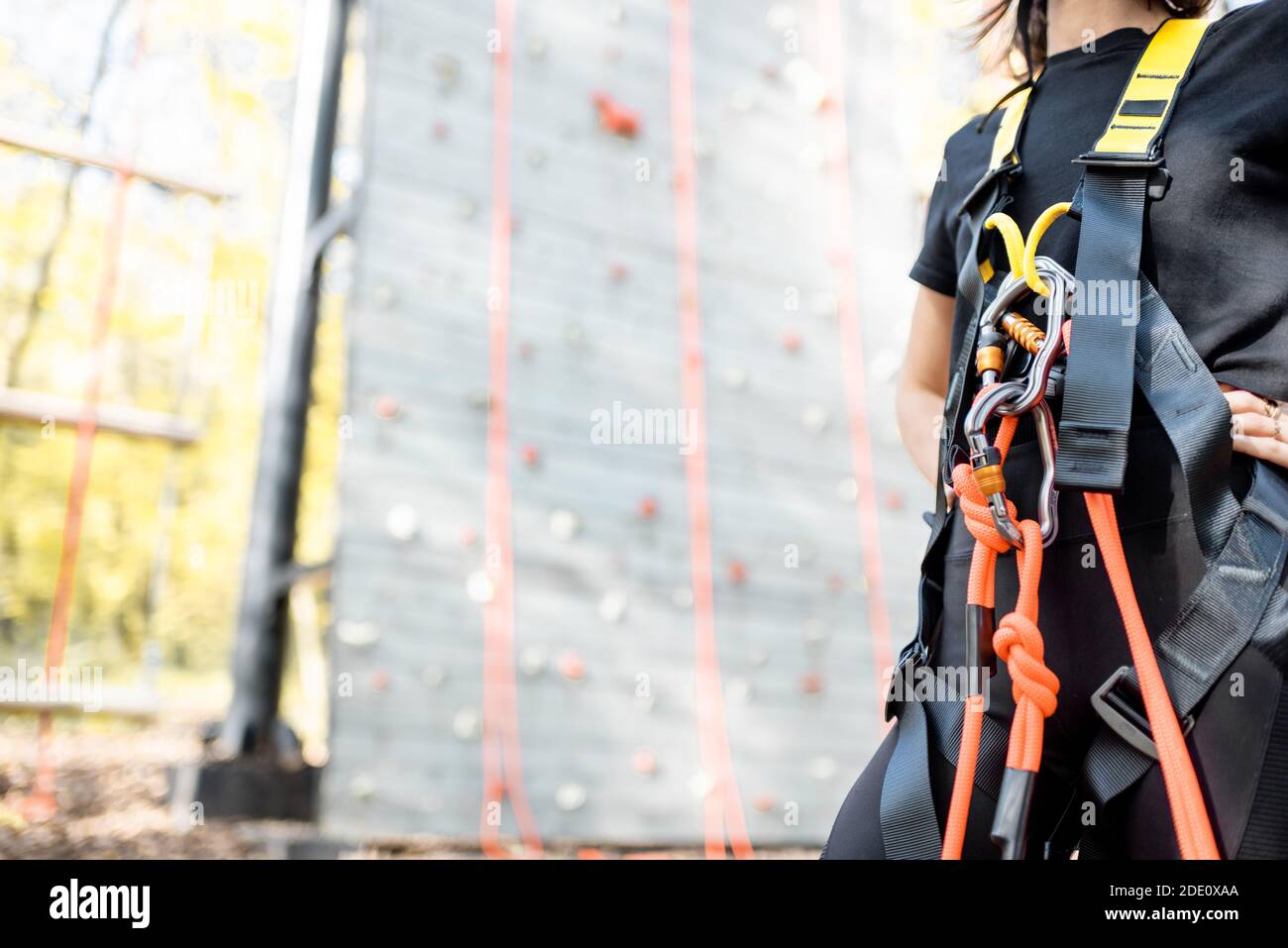 Primo piano delle attrezzature di sicurezza per gli scalatori indossati sulla donna con parete di arrampicata sullo sfondo Foto Stock