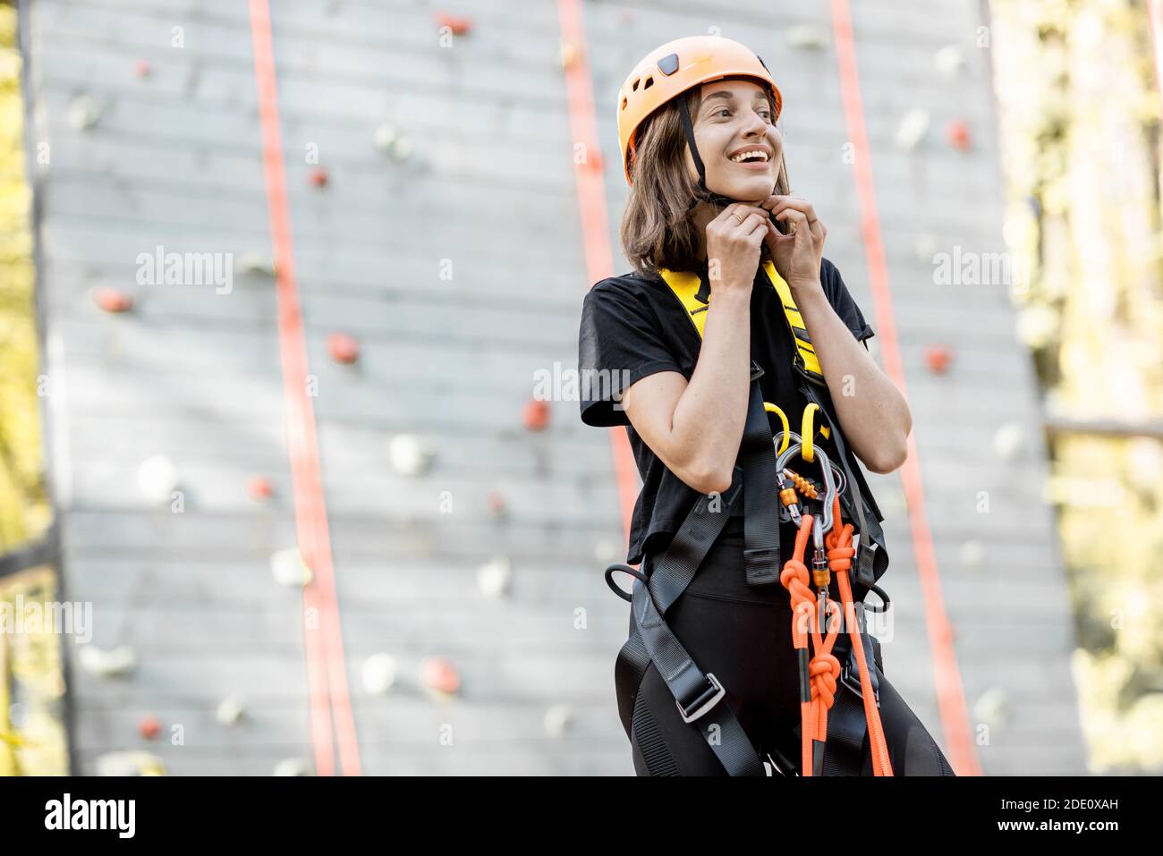 Ritratto di una giovane donna ben attrezzata in piedi davanti della parete di arrampicata al parco divertimenti Foto Stock