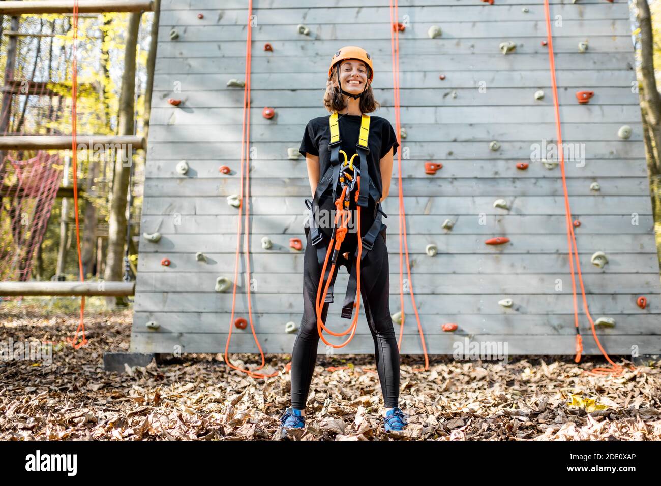 Ritratto di una giovane donna ben attrezzata in piedi davanti della parete di arrampicata al parco divertimenti Foto Stock