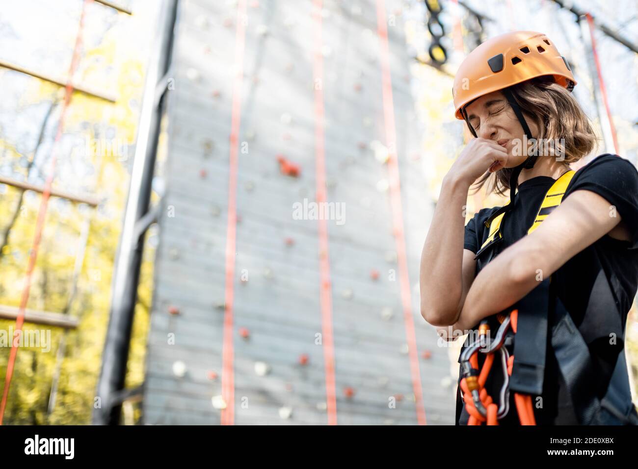 Ritratto di una giovane donna ben attrezzata che si sente spaventato prima di salire il muro al parco divertimenti. La donna ha paura delle altezze Foto Stock
