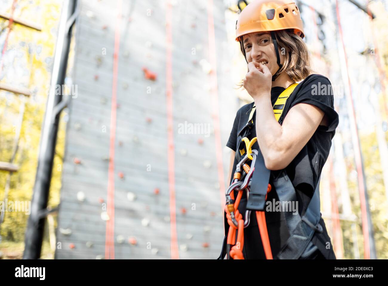 Ritratto di una giovane donna ben attrezzata che si sente spaventato prima di salire il muro al parco divertimenti. La donna ha paura delle altezze Foto Stock