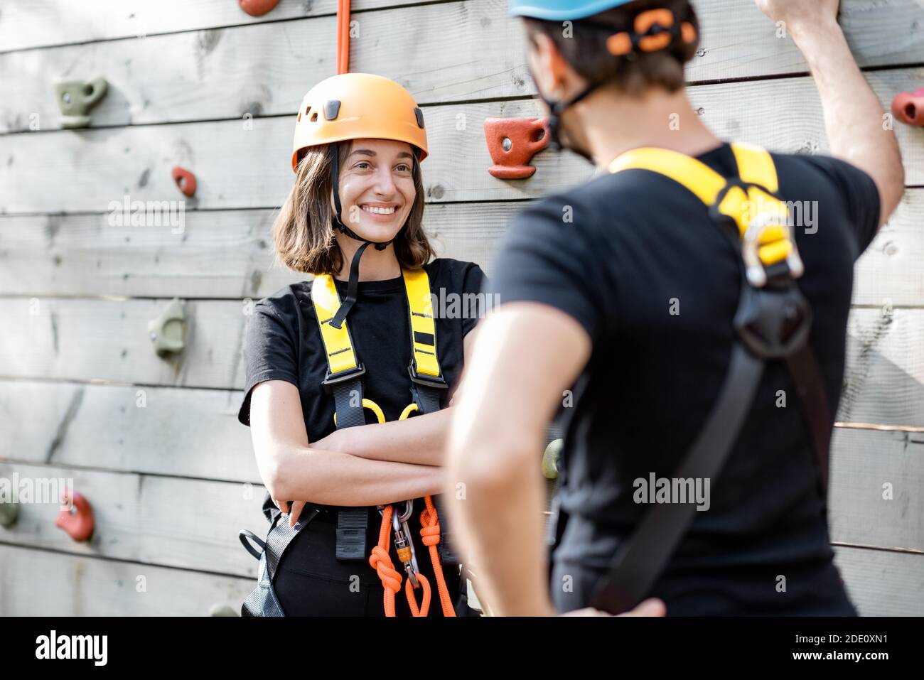 Sport Coppia ben attrezzata che parla e si diverte vicino alla parete di arrampicata, pronta per l'arrampicata al parco divertimenti Foto Stock