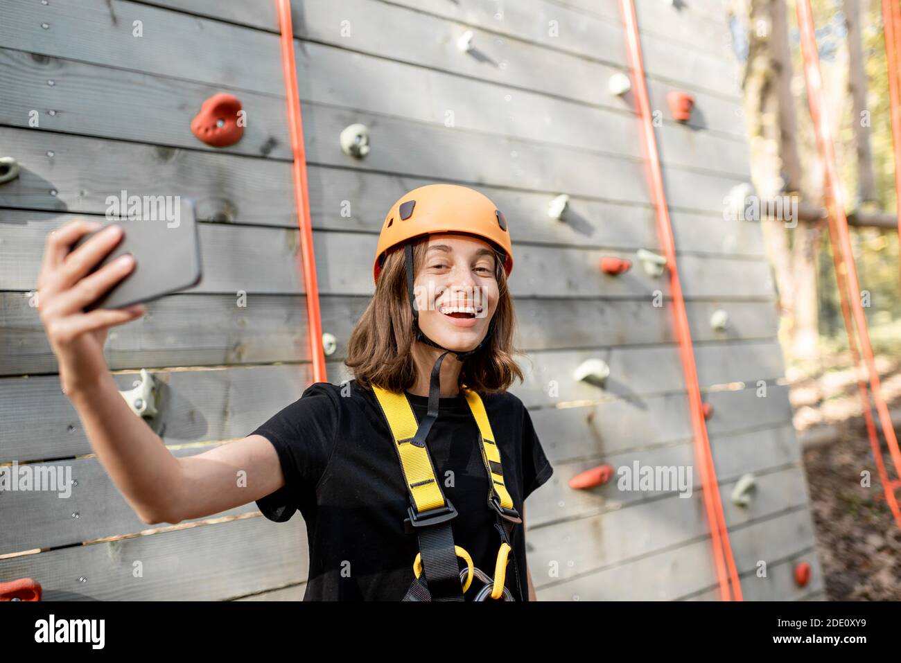 Giovane donna in attrezzature sportive protettive scattando una foto selfie con uno smartphone, giovane arrampicatore si sente felice nel parco per l'intrattenimento sportivo Foto Stock
