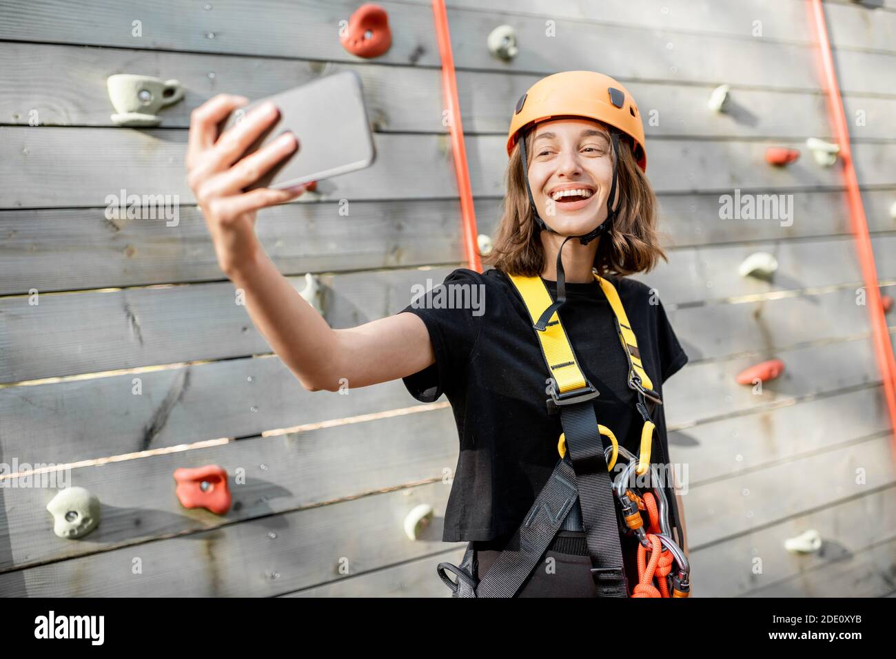 Giovane donna in attrezzature sportive protettive scattando una foto selfie con uno smartphone, giovane arrampicatore si sente felice nel parco per l'intrattenimento sportivo Foto Stock