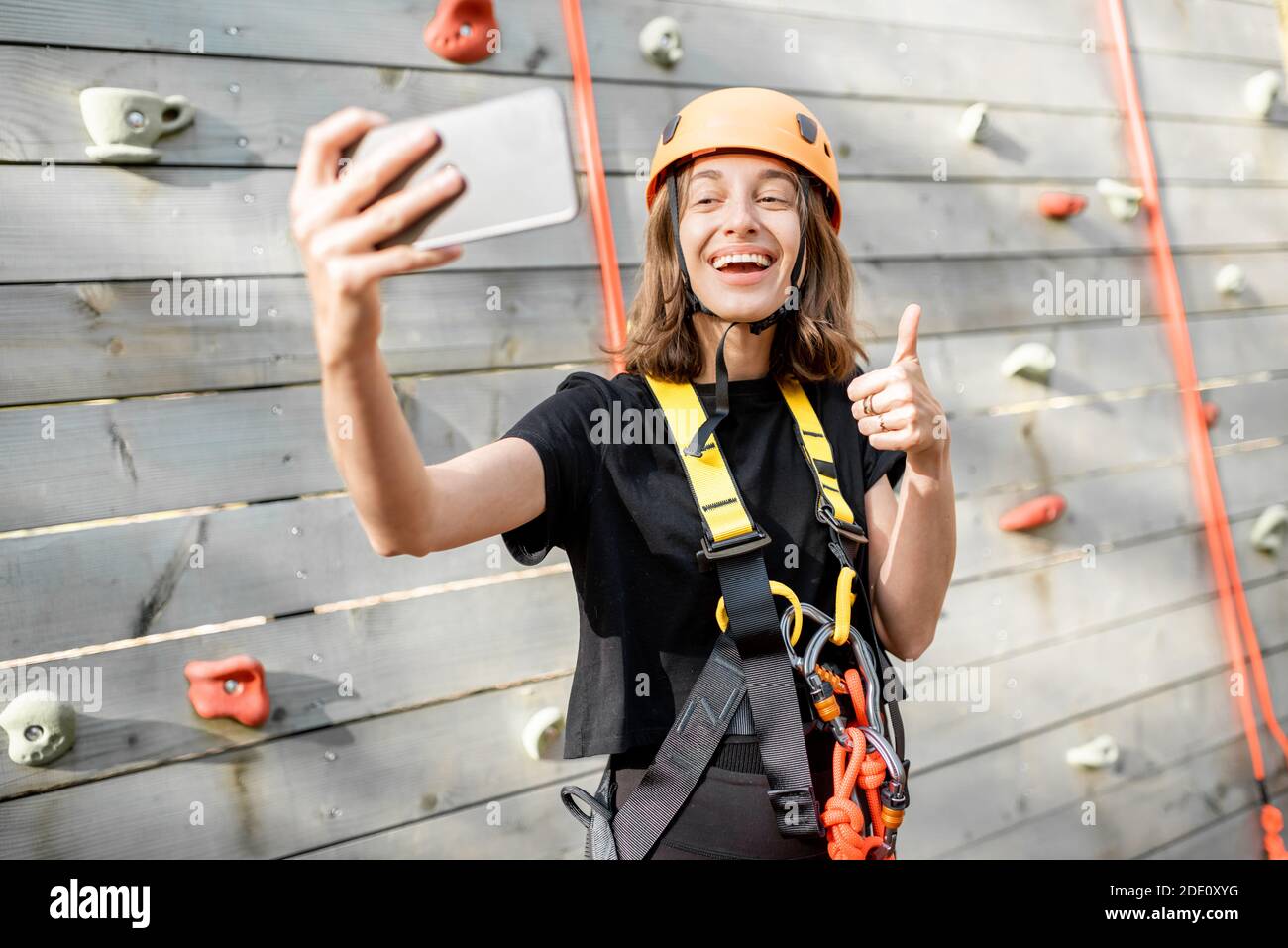 Giovane donna in attrezzature sportive protettive scattando una foto selfie con uno smartphone, giovane arrampicatore si sente felice nel parco per l'intrattenimento sportivo Foto Stock