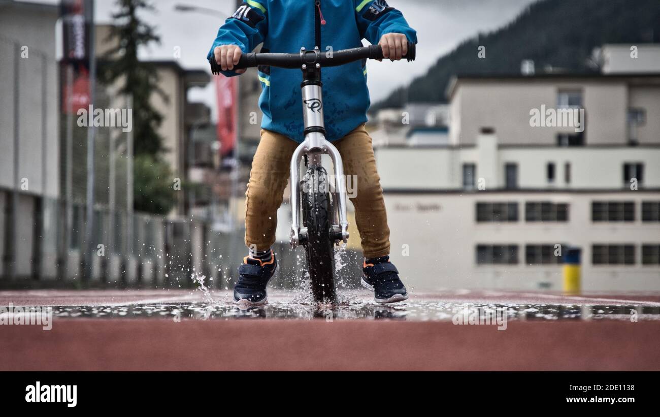 il bambino si diverte con la bici balance, il bambino felice gioca con una pozza d'acqua, pedalando in giovane età Foto Stock