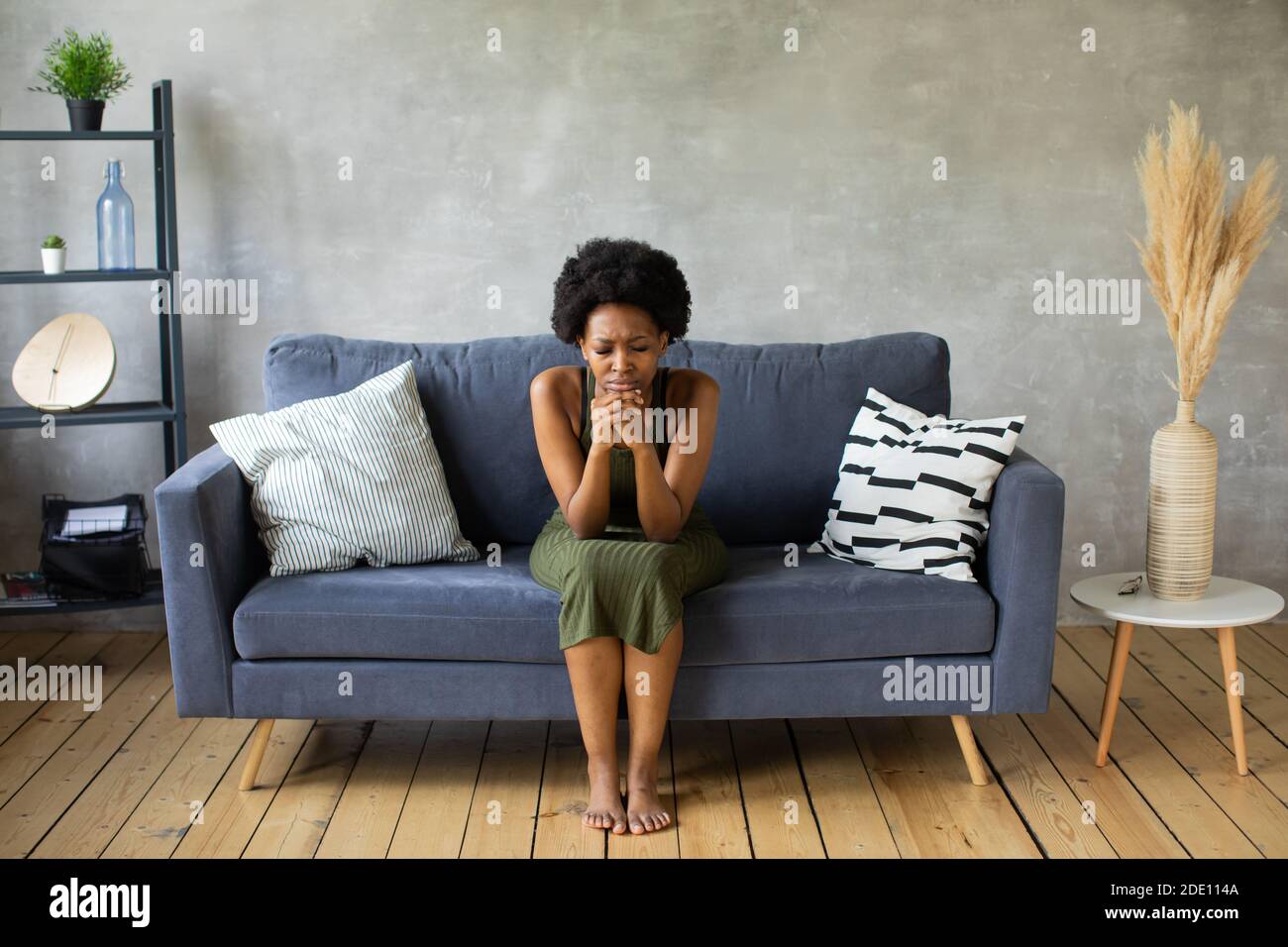 Infelice donna afroamericana siediti sul divano, la ragazza è molto turbata seduta sul divano del suo appartamento. Foto Stock