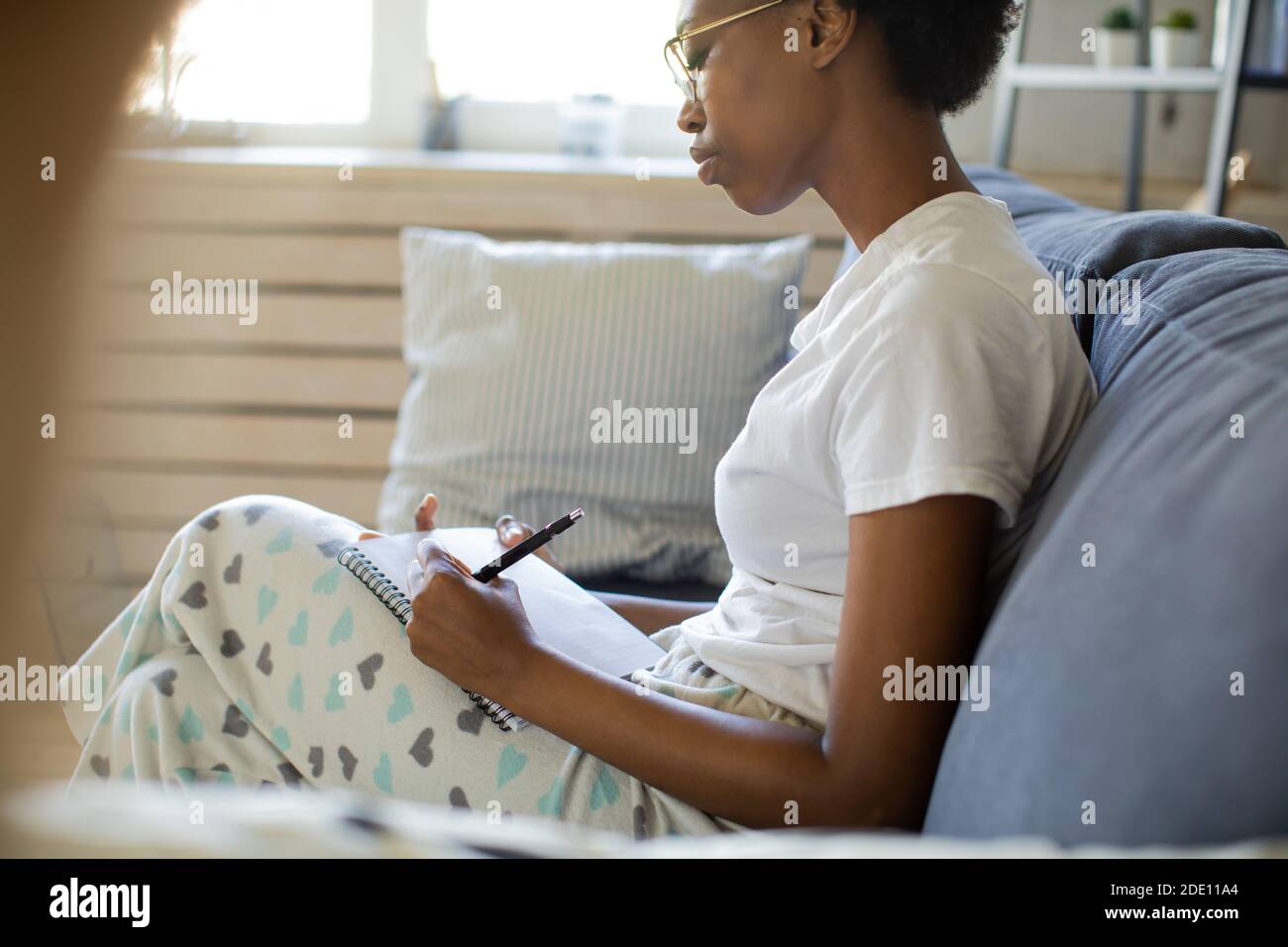 African American ragazza scrive in un notebook in un accogliente camera Foto Stock