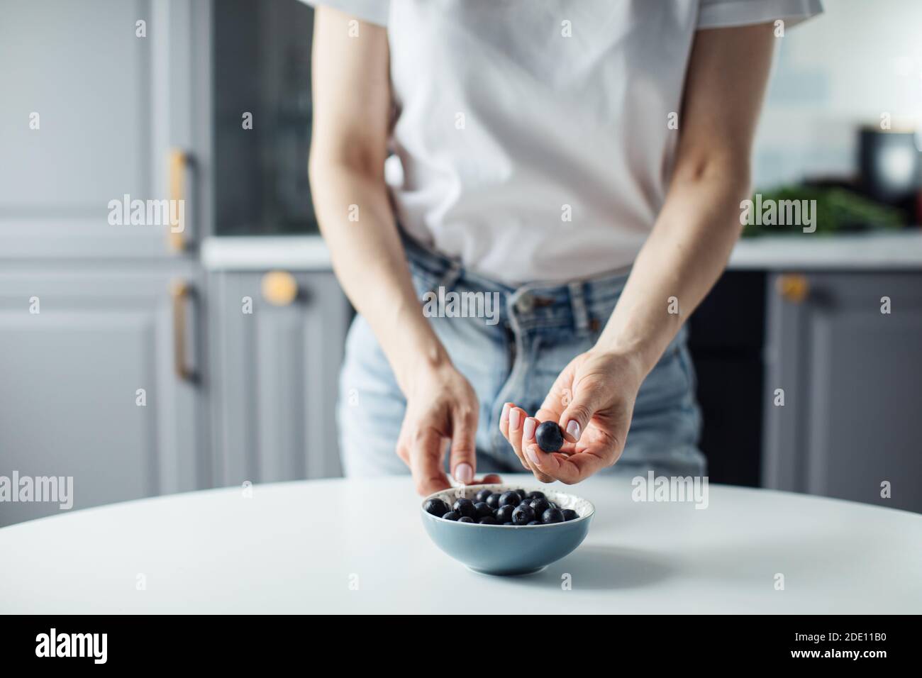 Le mani della donna prendono i mirtilli dal piatto. Sullo sfondo di una bella cucina. Foto Stock