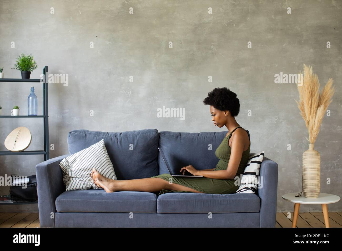 Felice african American giovane donna sedersi rilassarsi su un divano accogliente e lavorare su un computer portatile. Felice di trasferirsi in un nuovo appartamento Foto Stock