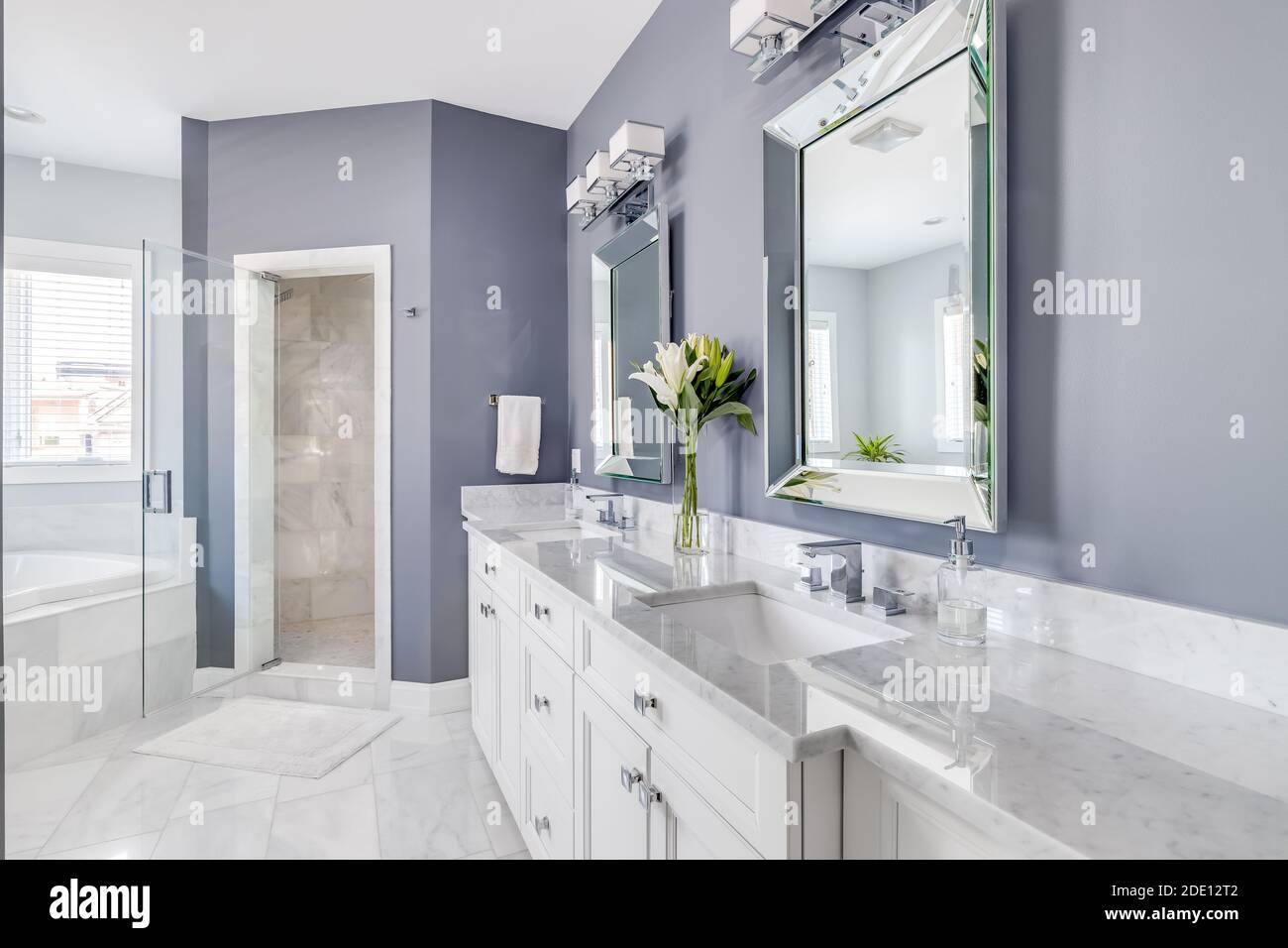 Una lussuosa stanza da bagno con pareti viola, un armadio bianco e un piano di lavoro, e dettagli in metallo cromato che guardano verso una cabina doccia piastrellata e una vasca idromassaggio. Foto Stock