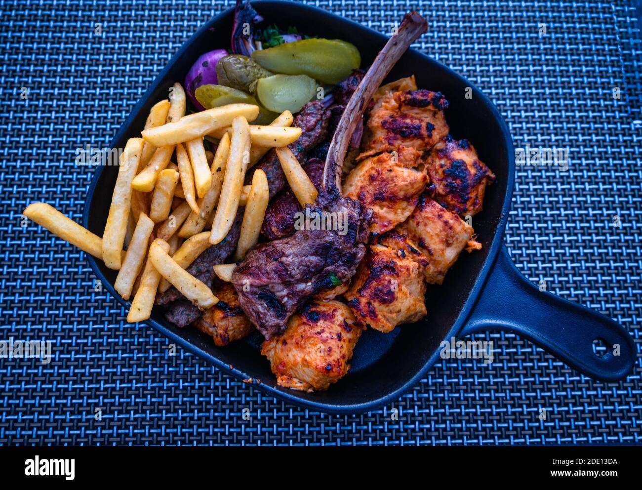 Turco tradizionale Ramadan Kebab Kofta con patatine fritte, cipolla, sottaceti e insalata in un piatto blu su sfondo blu. Foto Stock