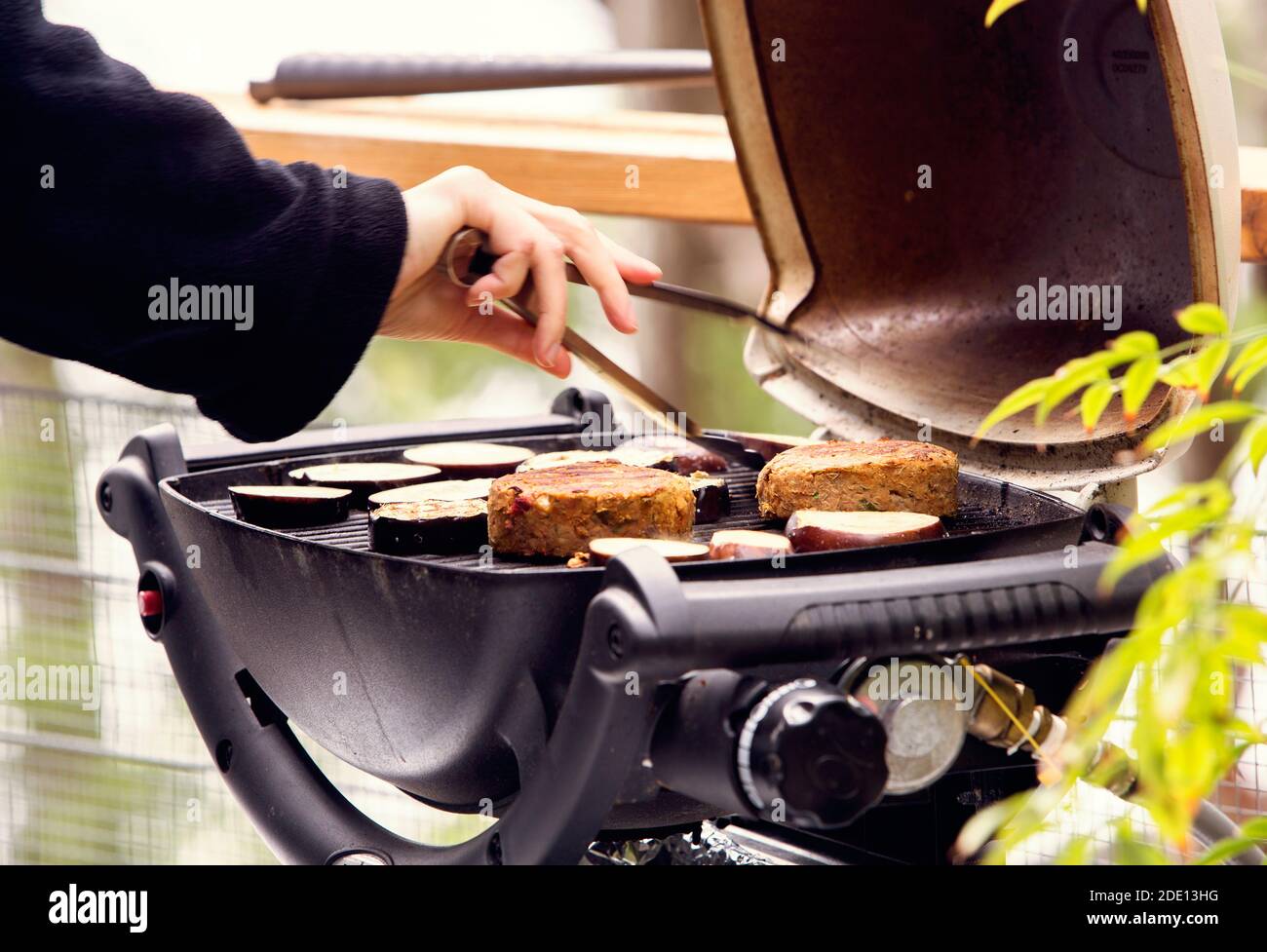 Le melanzane e gli hamburger vegetariani sono grigliati su un barbecue portatile e. in procinto di essere ruotato con le pinze Foto Stock