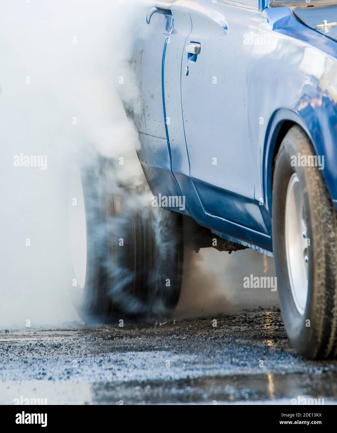 Auto che fa un burnout. Lo pneumatico posteriore gira molto velocemente e fa molto fumo. L'auto è blu ma non identificabile. Foto Stock