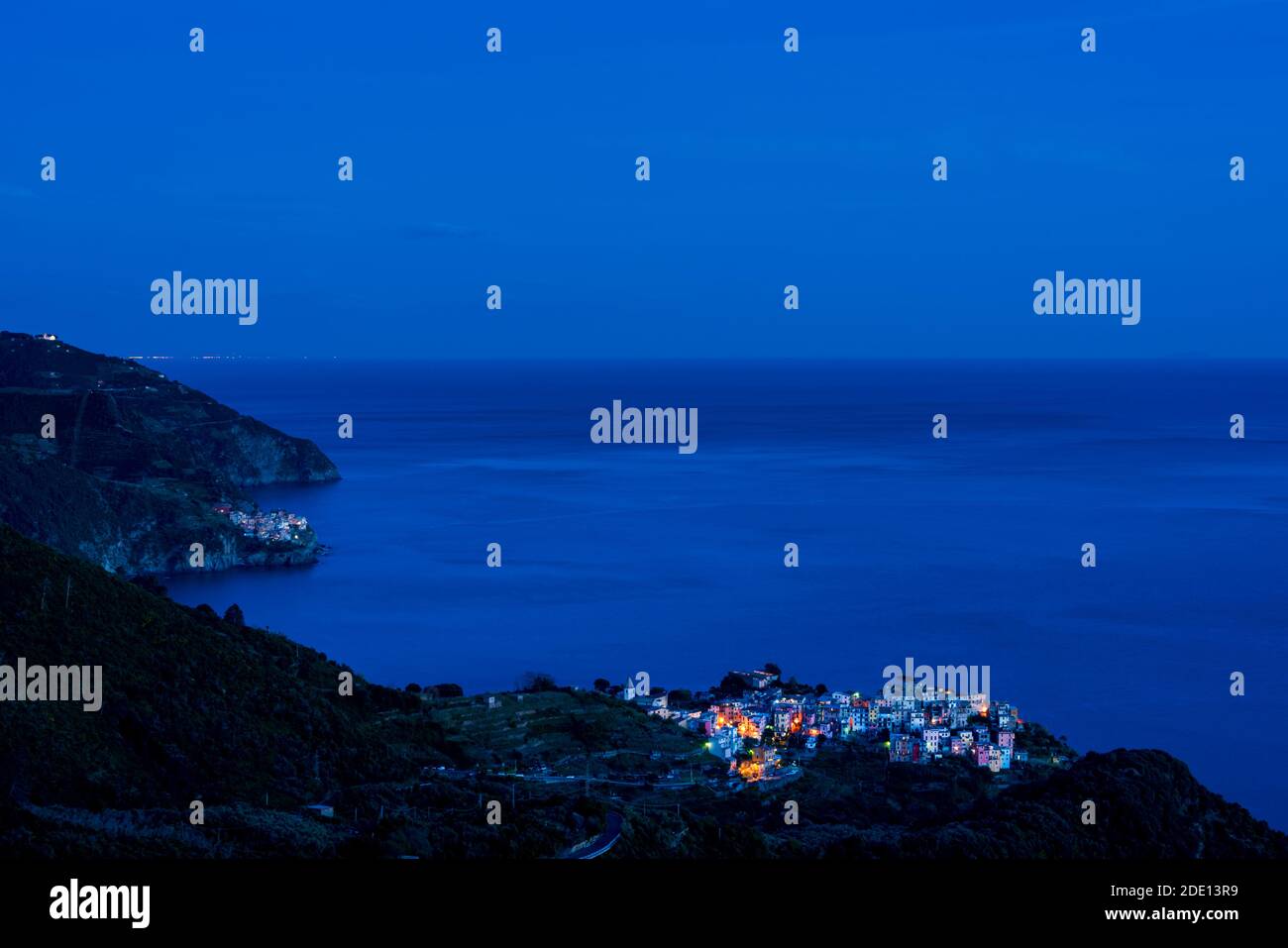 I villaggi di pescatori di Corniglia (fronte) e Manarola (indietro) nelle cinque Terre, illuminate al tramonto durante l'ora blu con il Mar Mediterraneo Foto Stock