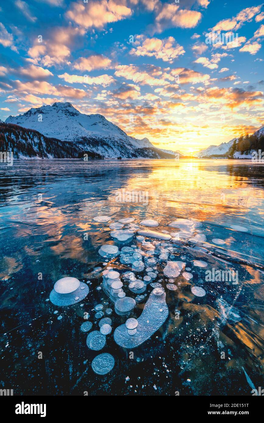 Nuvole nel cielo ardente al tramonto su Piz da la Margna e bolle di ghiaccio intrappolate nel lago Sils, in Engadina, in Graubunden, in Svizzera, in Europa Foto Stock