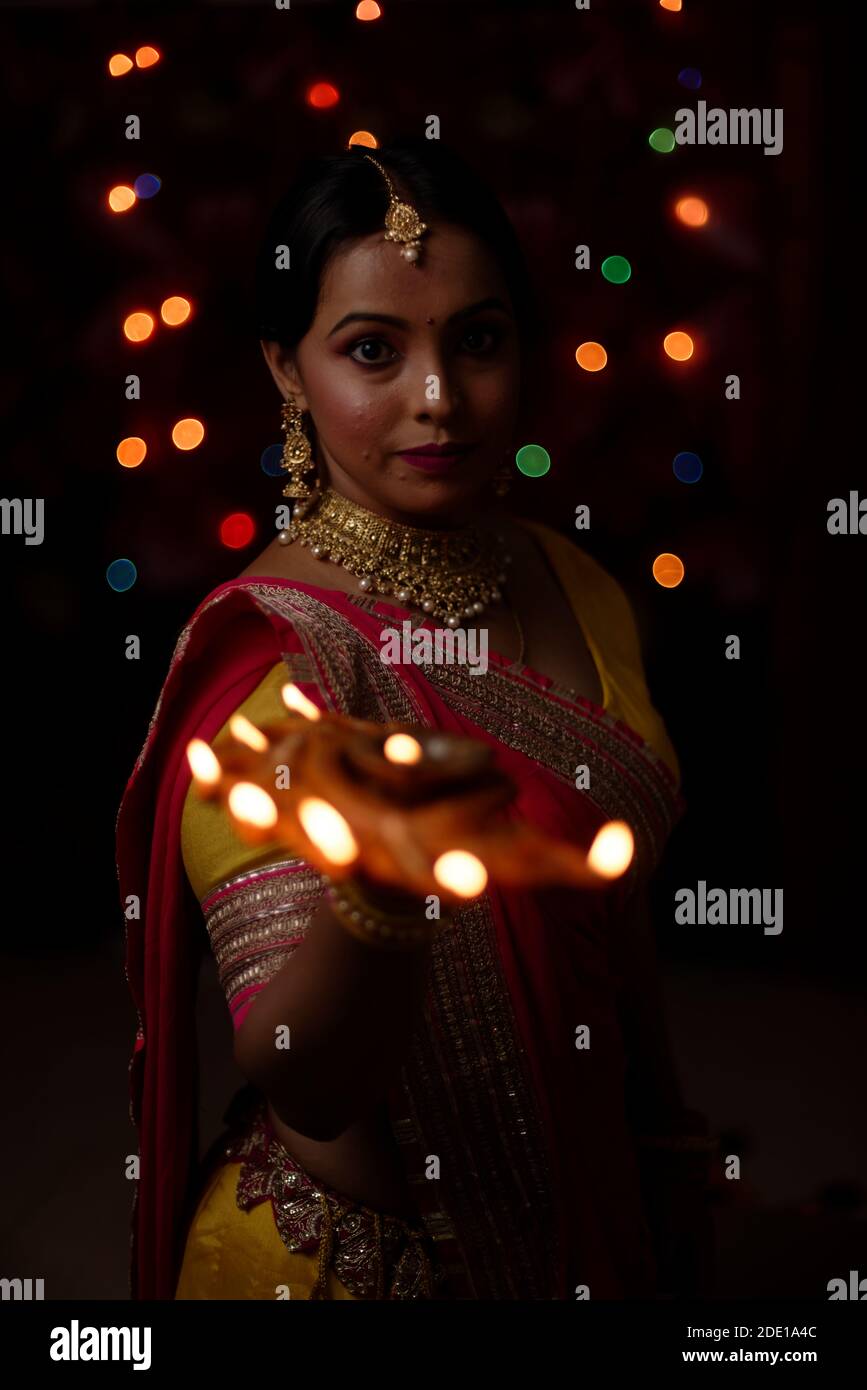 Una giovane e bella donna indiana bengalese in abito tradizionale indiano sta tenendo una Diwali diya / lampada in mano davanti a colorate luci bokeh. Foto Stock