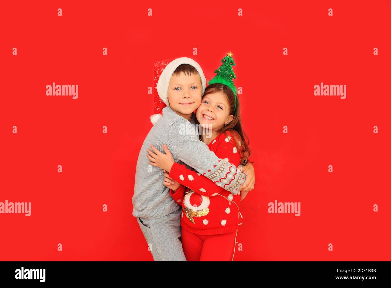 Ragazzo e ragazza nei maglioni di Capodanno su sfondo rosso. Due bambini che abbracciano gli abiti di Natale Foto Stock